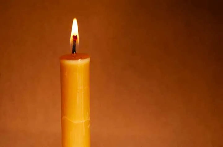 Bougie de cire d’abeille allumée sur fond orangé.
