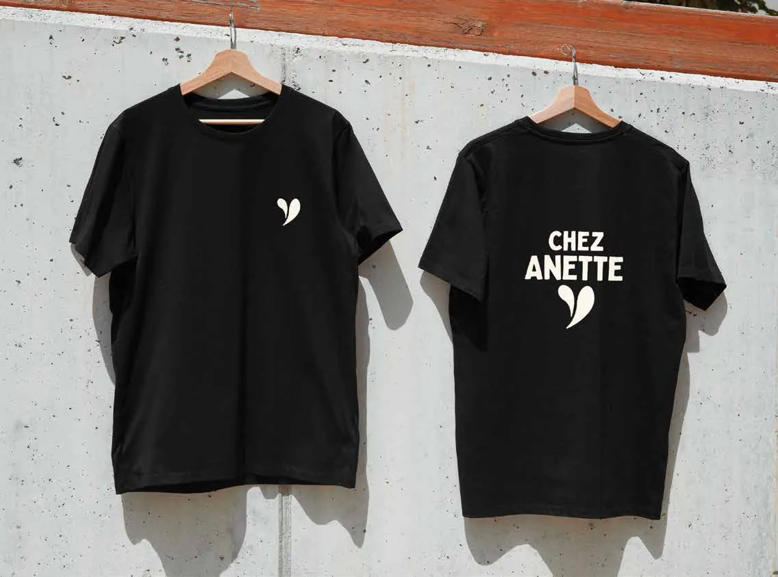 Deux t-shirts noirs suspendus, ornés du logo en forme de cœur stylisé de Chez Anette.
